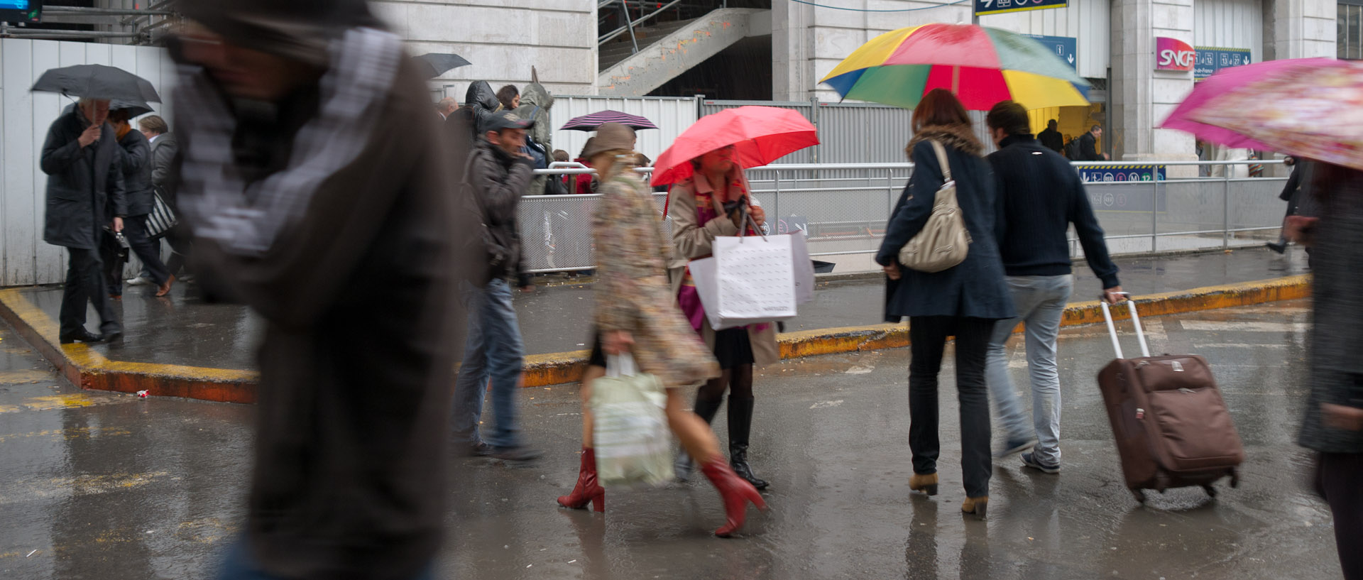 Passants sous la pluie, cour du Havre, gare Saint-Lazare, à Paris.