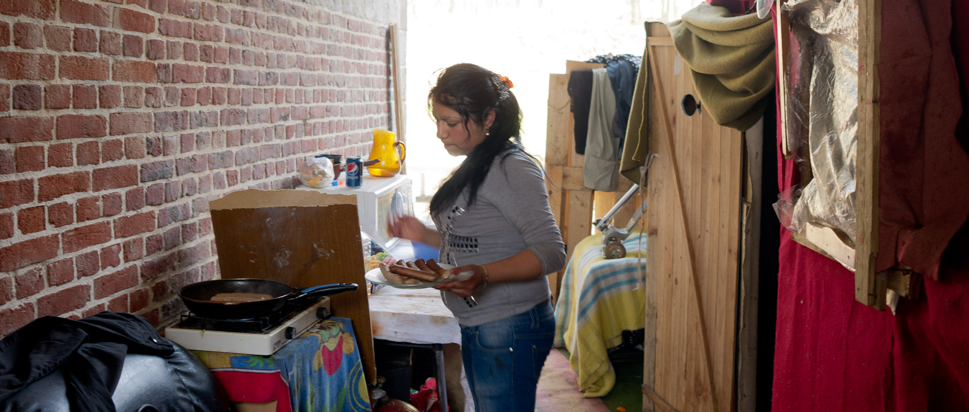 Femme cuisant des saucisse dans un campement de Roms, rue de Gand, à Lille.