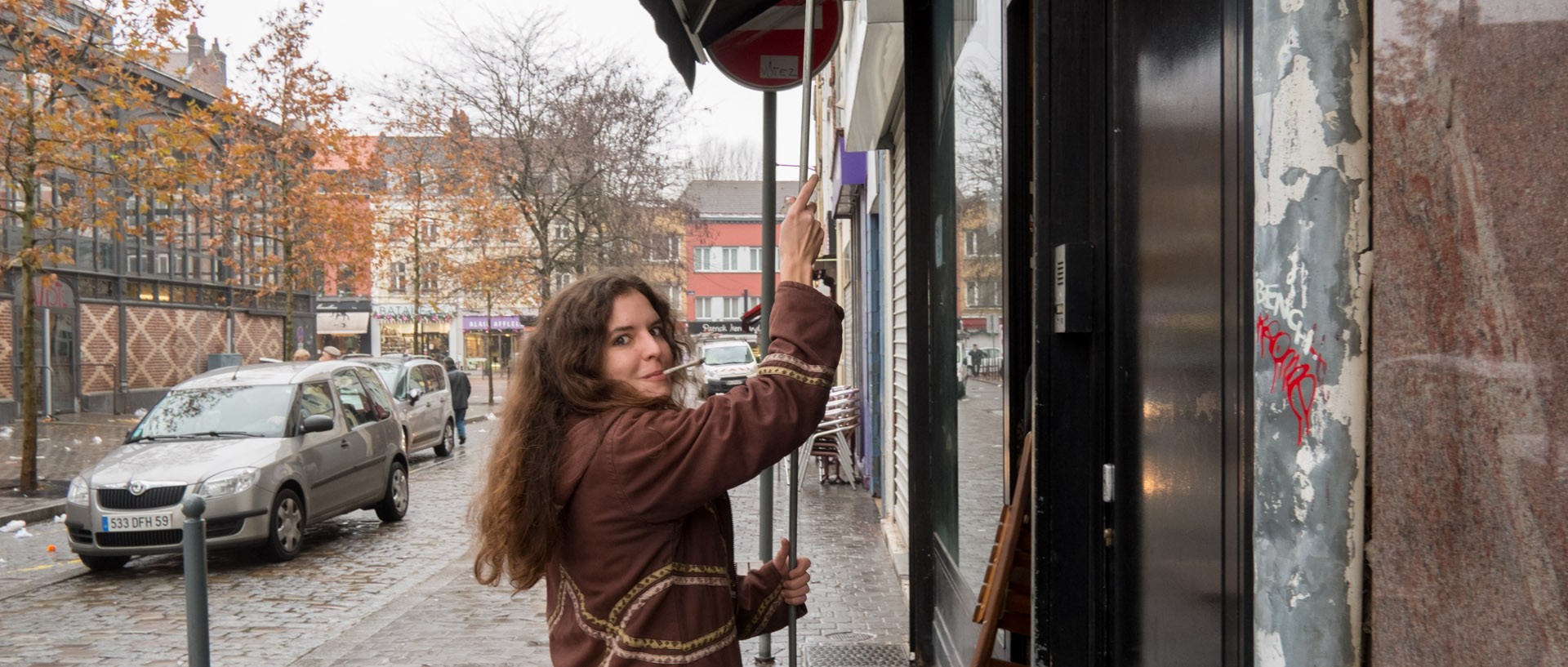 Jeune fille relevant le store d'un café, cigarette aux lèvres, place de la Nouvelle Aventure, à Wazemmes, Lille.