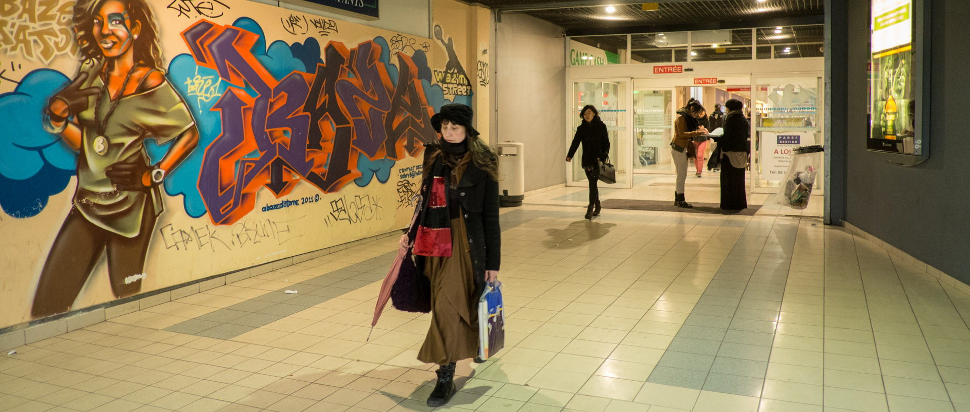 Femme marchant devant un mur tagué, dans un centre commercial, rue Gambetta, à Wazemmes, Lille.