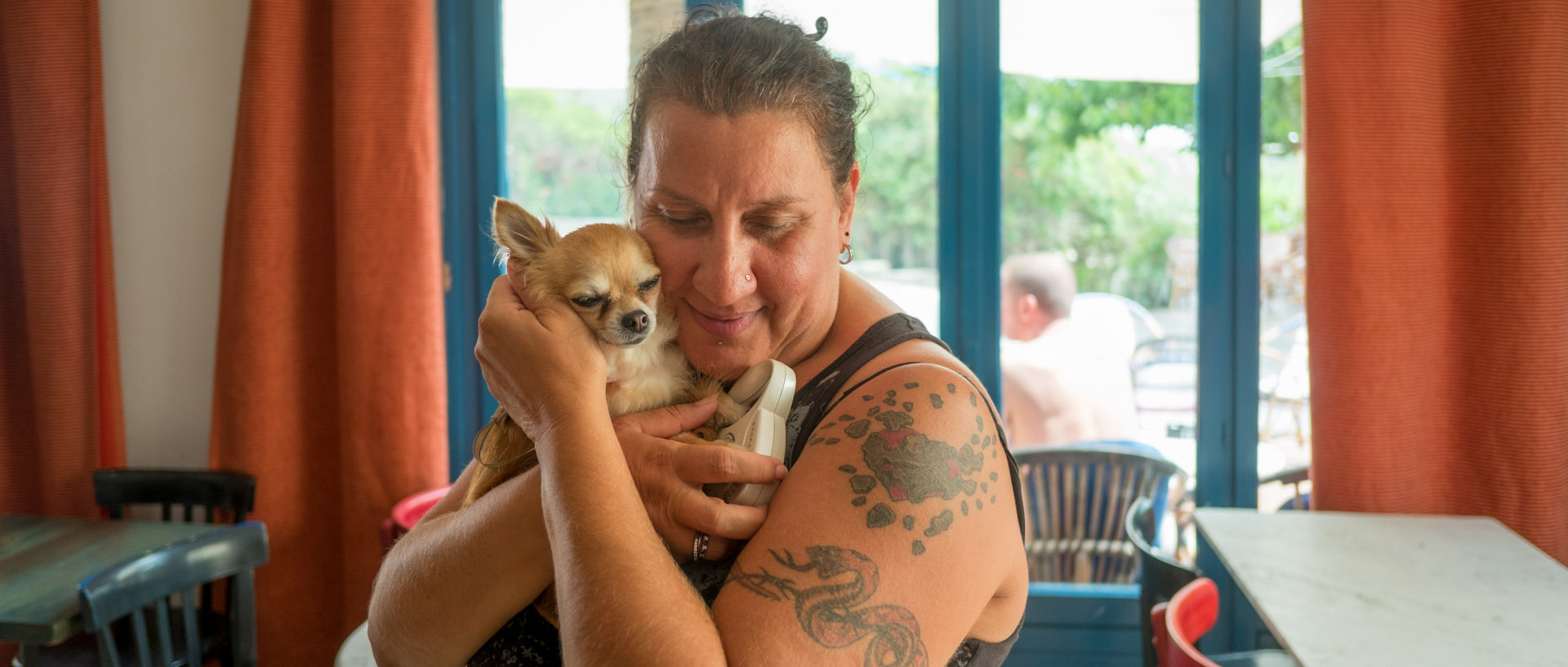 Martine tenant un chien dans ses bras, au bar de la Pomme d'Adam, à l'île du Levant.